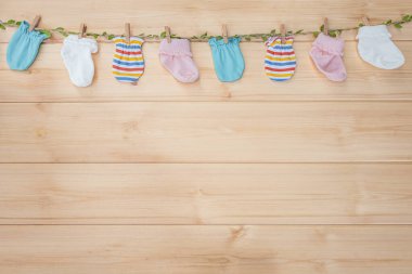 Ahşap arka planda çamaşır ipinde asılı renkli bebek çorapları. Çocuklar için pamuk aksesuarlar, bebek bakımı konsepti. Bebek eşyaları, yeni doğmuş eldivenler, bebek eldivenleri.