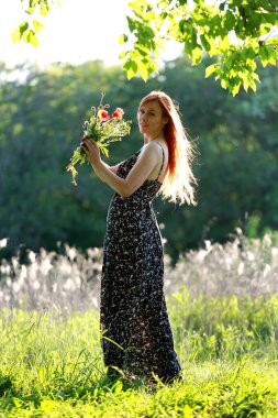 Yabani gelincikli bir kız nehir kenarındaki bir tepeden manzaranın tadını çıkarır. Neşe, mutluluk, huzur. Nehir kıyısında yabani gelincikler.