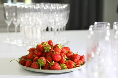 Beyaz bir masa örtüsü üzerinde bir tabakta çilek. Beyaz bir masada yuvarlak bir tabakta çilekler. Beyaz bir masa örtüsünün üzerinde, olgun ve tatlı çilekler..