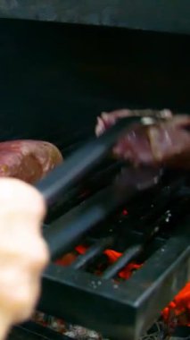 Izgarada biftek ve kömür pişiriyorum. Bir restoranda biftek kızartıyorum. Dikey video.