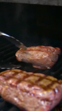 Izgarada biftek ve kömür pişiriyorum. Bir restoranda biftek kızartıyorum. Dikey video.