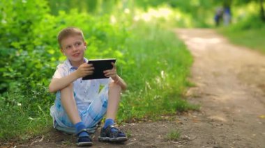 Bir çocuk parkta yürüyor ve bir tablette kulaklıkla müzik dinliyor..