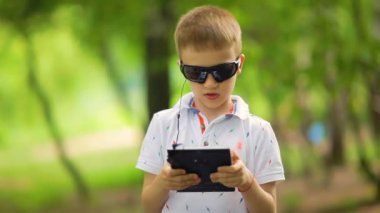 Video seti: Bir çocuk parkta yürüyor ve bir tablette kulaklıkla müzik dinliyor.