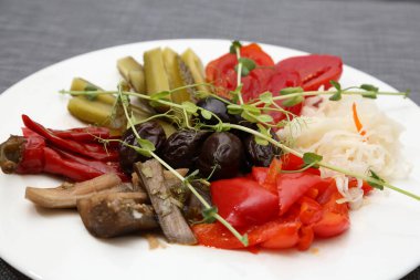 Salamura domates, lahana, salatalık, patlıcan, kırmızı biber, erik. Beyaz tabakta turşu. Restoranda çeşitli sebze turşusu servis ediyorlar.