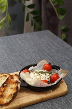 Domatesli peynirli ızgara peynir ve kızarmış ekmek. Ahşap bir tahtanın üzerinde ızgara tavasında camembert peyniri.