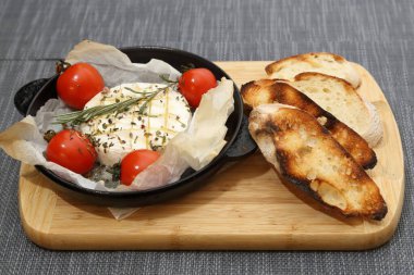 Domatesli peynirli ızgara peynir ve kızarmış ekmek. Ahşap bir tahtanın üzerinde ızgara tavasında camembert peyniri.