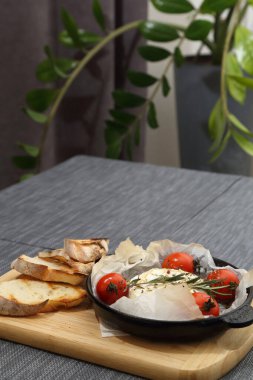 Domatesli peynirli ızgara peynir ve kızarmış ekmek. Ahşap bir tahtanın üzerinde ızgara tavasında camembert peyniri.