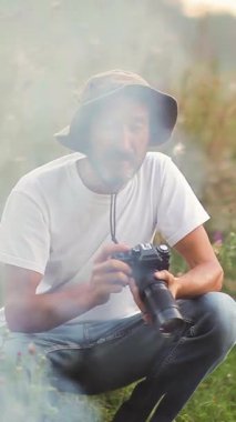 Erkek fotoğrafçı vahşi doğada gün batımında güzel bir manzara yaratıyor. Açık havada çalışan bir fotoğrafçı. Fotoğraf avı. Akşam güneşinde işini yapan bir fotoğrafçı. Dikey video.