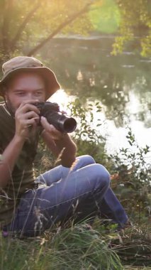 Erkek fotoğrafçı vahşi doğada gün batımında güzel bir manzara yaratıyor. Açık havada çalışan bir fotoğrafçı. Fotoğraf avı. Akşam güneşinde işini yapan bir fotoğrafçı. Dikey video.