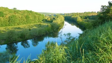 Nehir kenarındaki muhteşem yaz doğası. Yazın gün batımında güneş ışığında güzel bir nehir. Nehrin sakin akışı. Nehir kıyısındaki yaban çiçekleri.