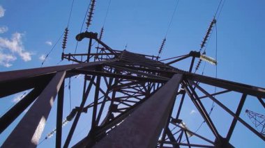 Elektrik iletimi kablolarla yapılıyor. Mavi gökyüzü ve uçan bulutların arka planında kablolar ve yalıtıcılarla yüksek voltaj destekliyor. 