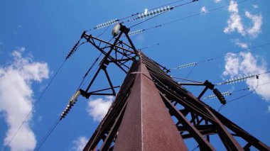 Elektrik iletimi kablolarla yapılıyor. Mavi gökyüzü ve uçan bulutların arka planında kablolar ve yalıtıcılarla yüksek voltaj destekliyor. 