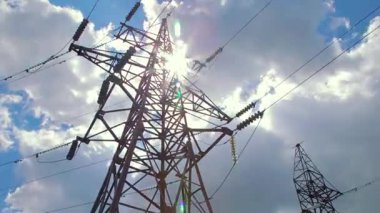 Elektrik iletimi kablolarla yapılıyor. Mavi gökyüzü ve uçan bulutların arka planında kablolar ve yalıtıcılarla yüksek voltaj destekliyor. 