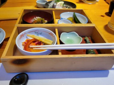 Sebze ve baklagiller de dahil olmak üzere çeşitli yiyeceklerin sunulduğu geleneksel Japon yemeği ahşap bir kutuda sunuldu ve yanında Japonya 'daki samimi geleneksel bir Japon restoranında bir çift hashi çubuğu servis edildi..