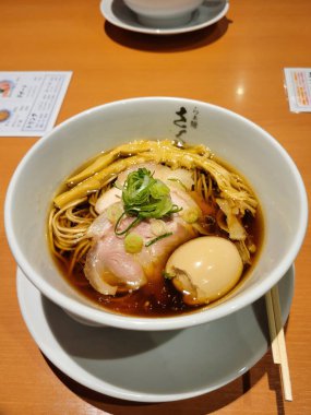 Haşlanmış yumurta ve sulu domuz dilimleriyle servis edilen ağız sulandırıcı sıcak ramen eriştesi, Japonya 'da rahat bir restoranda geleneksel Japon yemek çubukları (hashi) eşliğinde..