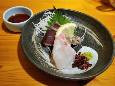 Bir dilim sebze, bir dilim limon, bir tutam wasabi ve Japonya 'daki geleneksel bir Japon restoranında servis edilen bir kase baharatlı soya sosu eşliğinde taze çiğ balığın eşlik ettiği narin ve ferahlatıcı bir sashimi tabağı..