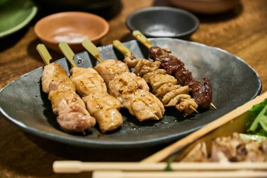 Yakitori ahşap bir masada bir tabakta servis yapıyordu. Mükemmel ızgara tavuk ve domuz şişleri tüm ihtişamıyla sunuluyor, rahat ve dost canlısı bir atmosferle çevrili..