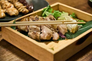 Tavuk yakitori ahşap bir kutuda servis edilir ve üzerinde Japon yemek çubukları (hashi))