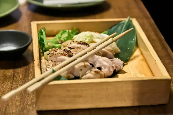 stock image Chicken yakitori served in a wooden box and on top of it your Japanese chopsticks (hashi)