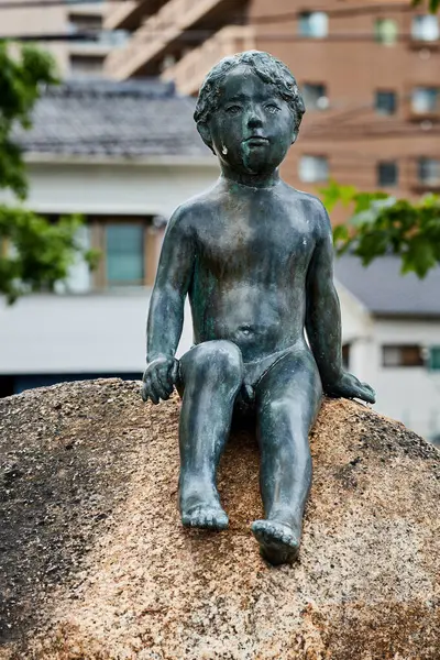 stock image OKAYAMA, JAPAN - MAY 22 2023: A charming statue of a boy sitting on a stone, located along the path to Okayama Castle, Japan. 