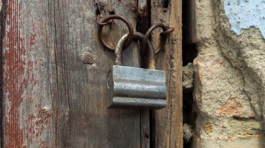 Eski demir asma kilit. Asma kilit parantezlerde asılı. Tahta kapı ve kilit