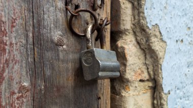 Eski demir asma kilit. Asma kilit parantezlerde asılı. Tahta kapı ve kilit