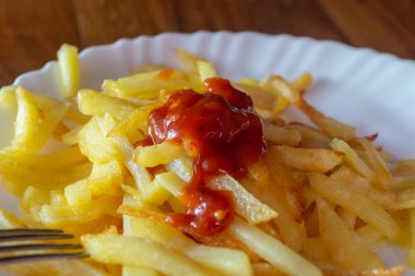 Beyaz bir tabakta yakın plan patates kızartması. Domates soslu kızarmış patates.