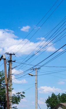 Sokak direkleri ve mavi gökyüzünün arka planında bir lamba. Elektrik direkleri ve kabloları cadde boyunca gerilmiş.