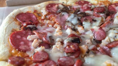 Karton kutuda sosisli, mantarlı ve peynirli pizza. Karton bir kutuda etli pizza.