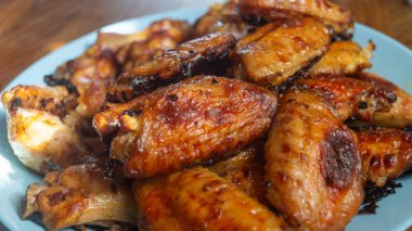 Fırında pişirilmiş tavuk kanatları ahşap bir masada yakın plan bir tabakta.