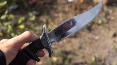 Bir insan elinde bir bıçak tutar. Arka planda geniş bir bıçak vardır. Yakın plan.