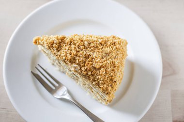 Piece of honey cake Medovik, layer cake on white plate and a fork. Top view.