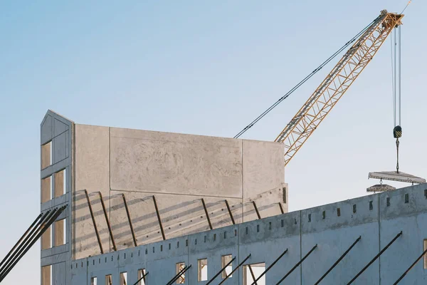 Güneşli bir günde inşaat alanında yeni bir binanın beton çerçevesinin arkasında sarı bir vinç.