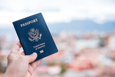 Bulanık bir arkaplan önünde mavi bir Amerikan pasaportu tutan tek bir el.