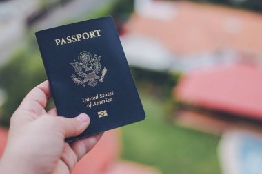 Bulanık bir arkaplan önünde mavi bir Amerikan pasaportu tutan tek bir el.
