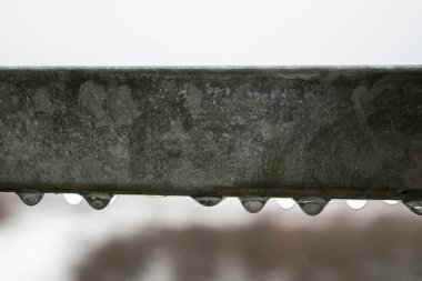 View of water droplets hanging from a metal railing on a rainy day