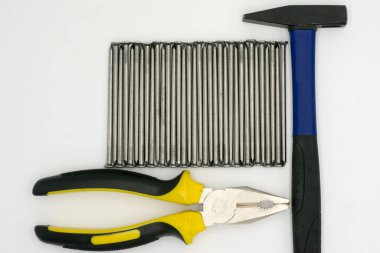 Metal çiviler, lacivert çekiç, beyaz arka planda sarı kerpeten.