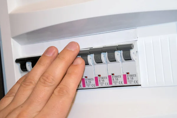 The fuse box is open, a man\'s hand turns off the fuse