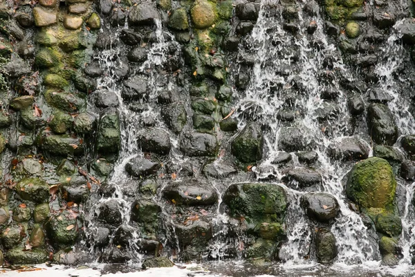 View of a stone wall and water flowing down the wall, a waterfall