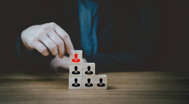 Businessman hold wood block leader person icon. Leadership in business concept. Hand pick a wooden cube block with red people icon out of black for talent, leadership, outstanding and right candidate.