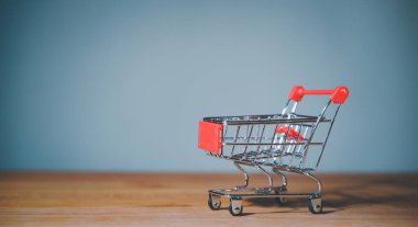 Shopping cart trolley on wood table blue background. Concept e-commerce, marketplace, buy or purchase grocery online store, retail business, consumer empty basket, shipping service, order payment