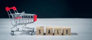 Ahşap blok ve beyaz ahşap arka planda boş alışveriş arabası satışı. Konsept perakende e-ticaret çevrimiçi mağazası, tanıtım indirimi, Kara Cuma, ticari tüketim ürünü reklamı.