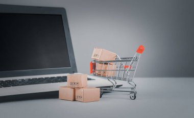 İnternetten alışveriş, ev teslimatı. Masa başında dizüstü bilgisayarı olan alışveriş arabasında kahverengi karton kutular. Tüketiciler için parmak uçlarıyla kolay alışveriş. e-ticaret ve müşteri deneyimi kavramı.