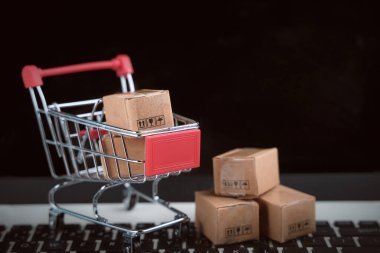 İnternetten alışveriş, ev teslimatı. Masa başında dizüstü bilgisayarı olan alışveriş arabasında kahverengi karton kutular. Tüketiciler için parmak uçlarıyla kolay alışveriş. e-ticaret ve müşteri deneyimi kavramı.