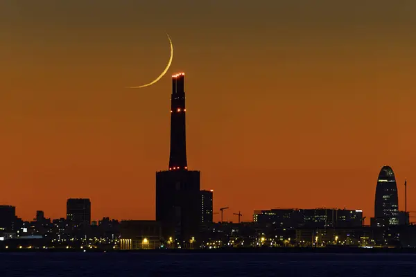 Her biri 200 metre uzunluğunda üç bacası olan eski bir termik santralin% 2 'sinde ay batımı azalıyor. Bu bacalar Barselona siluetinin bir parçası..