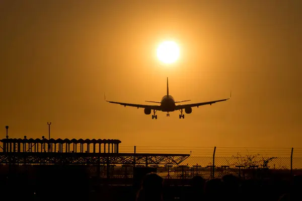 Bir uçağın inişi silueti. Gökyüzü tamamen turuncu çünkü güneş batıyor ve şimdiden çok alçak. Uçağın altında büyük siyah bir anten de görebilirsiniz..
