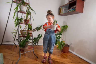 Ev bitkileriyle dolu bir odada çiçekleri sulayan küçük bir kız. Bitki bakımı ve sürdürülebilir yaşam