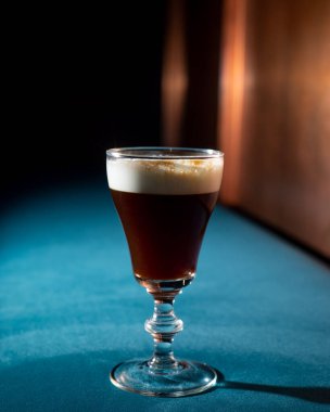 Brown cold brew coffee cocktail with cream and ice on a dark velvet background.