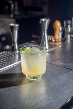 Yellow cocktail with lime and ice on the bar. Nightlife concept