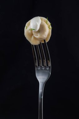 Cooking dumplings with sour cream on a fork on a black background